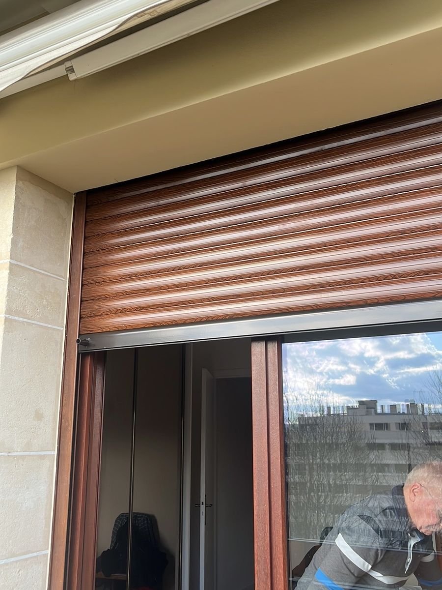 Volet roulant coloris bois installé sur la porte-fenêtre d'un balcon – dépannage volet roulant à Lassy